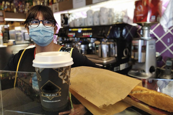 a woman wearing a mask working behind the counter of a cafe