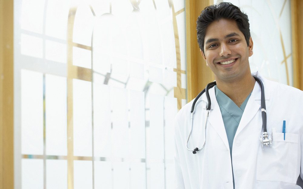 Indian or South Asian doctor standing against a bright window