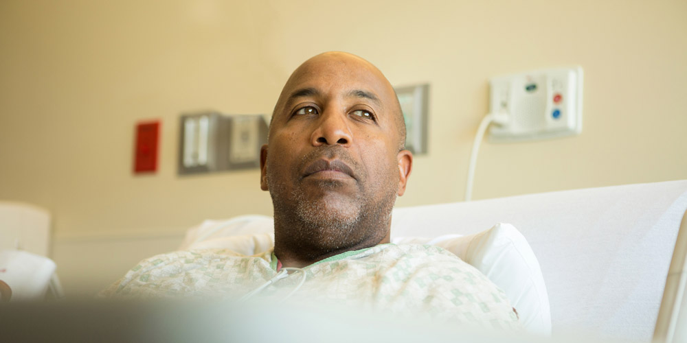 An African-American man sitting up in a hospital bed, looking thoughtful