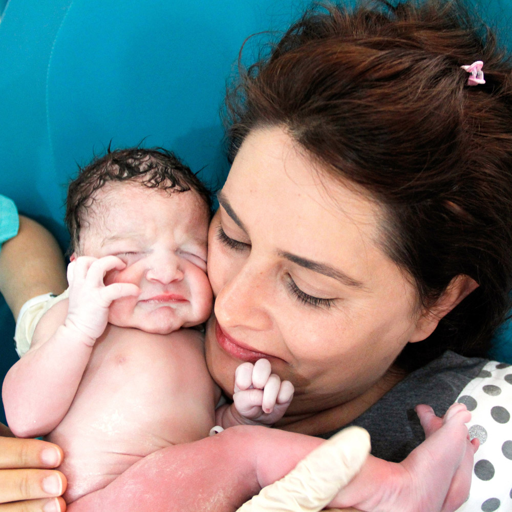 A mother who has just given birth holding her newborn baby close to her face with the help of a nurse or doctor
